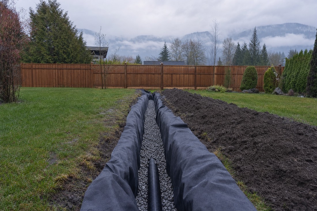 French drain gravel trench with perforated pipe and filter fabric crossing a Fraser Valley lawn